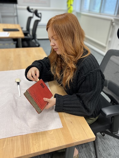 Person in grey jumper sat on an office chair carefully handling an old book