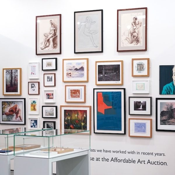 A white gallery wall with multiple framed pictures and a display case in front of it containing small objects