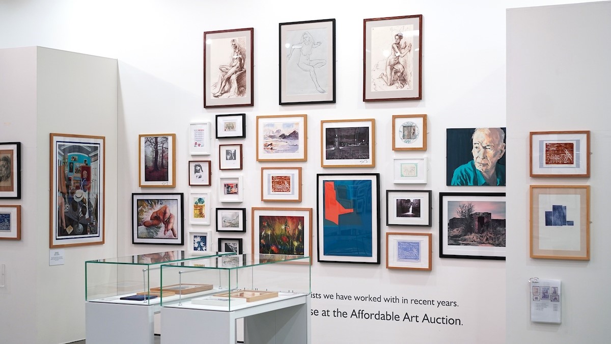 A white gallery wall with multiple framed pictures and a display case in front of it containing small objects