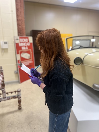 Person holding clipboard in front of museum objects
