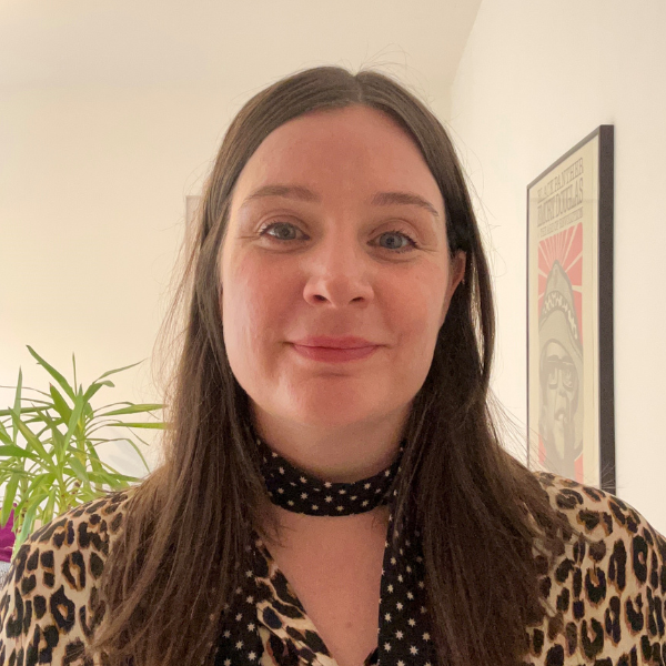 A woman with brown hair. She wears a scarf and a leopard print shirt